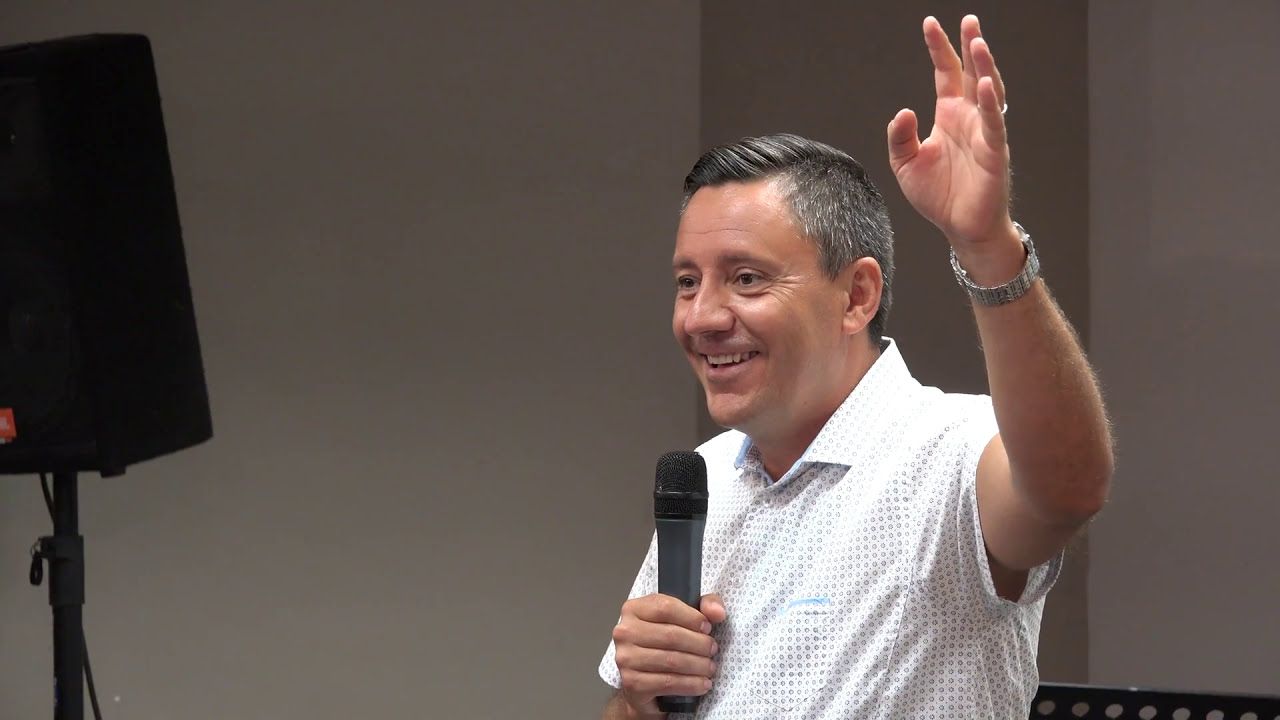 Ruslan Murin smiling and raising one hand while holding a microphone.