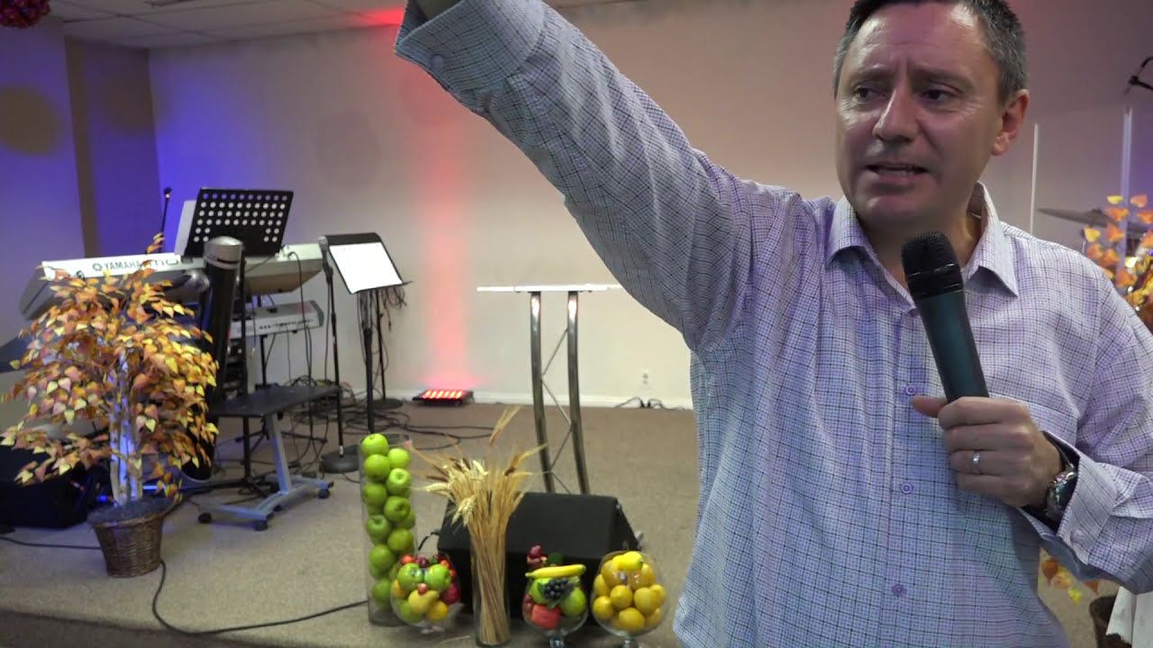 Ruslan Murin preaching with a microphone in one hand and the other arm raised high.
