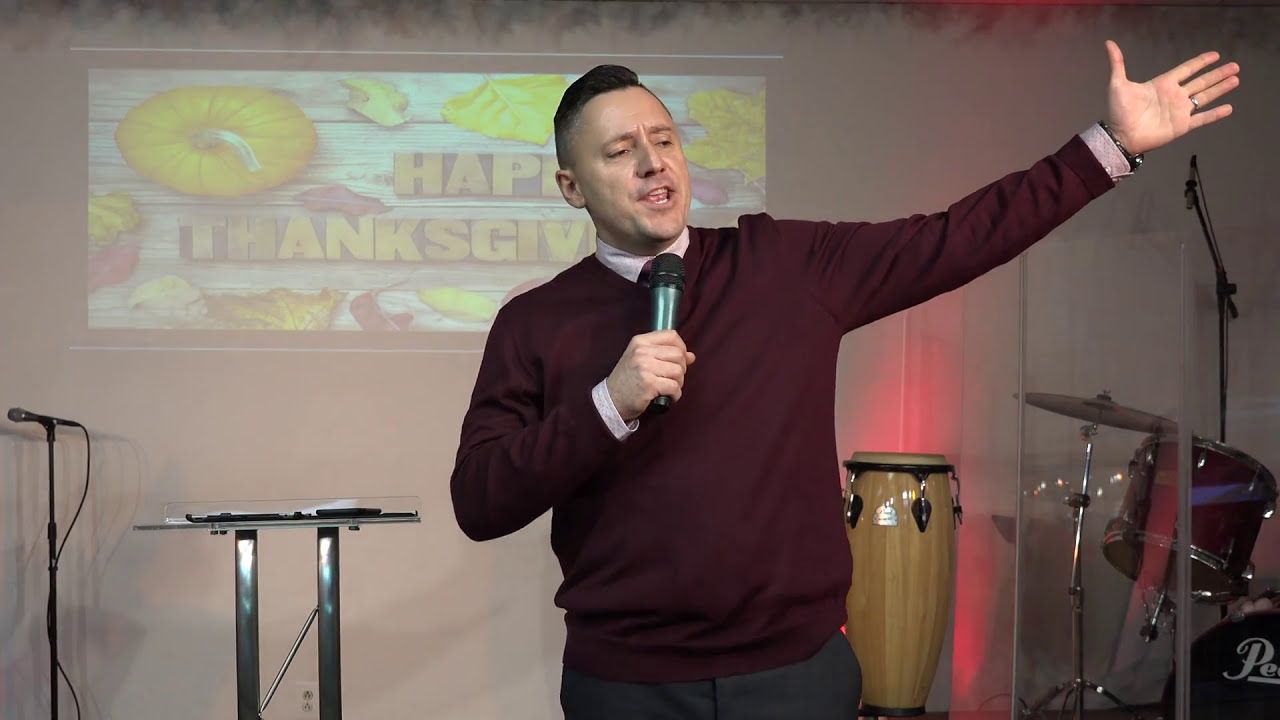 Ruslan Murin in a maroon sweater preaching into a microphone, one arm stretched out to the side.