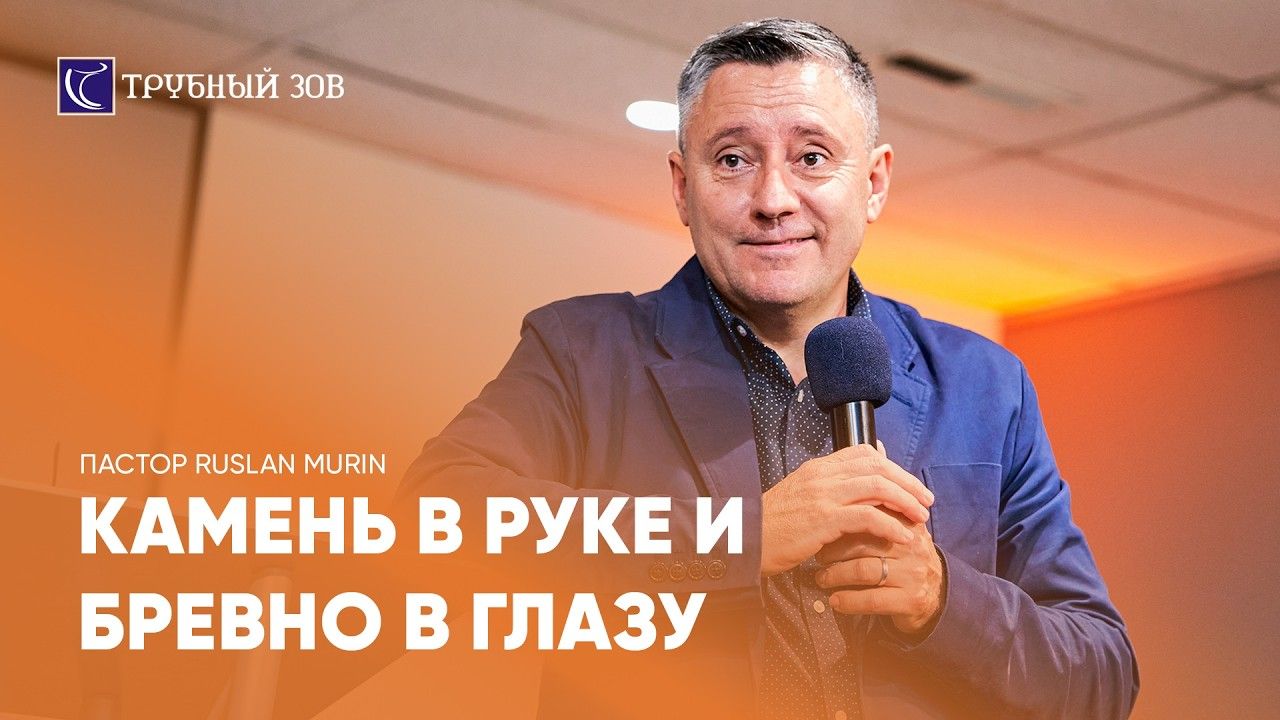 Pastor Ruslan Murin in a blue jacket, holding a microphone with both hands.
