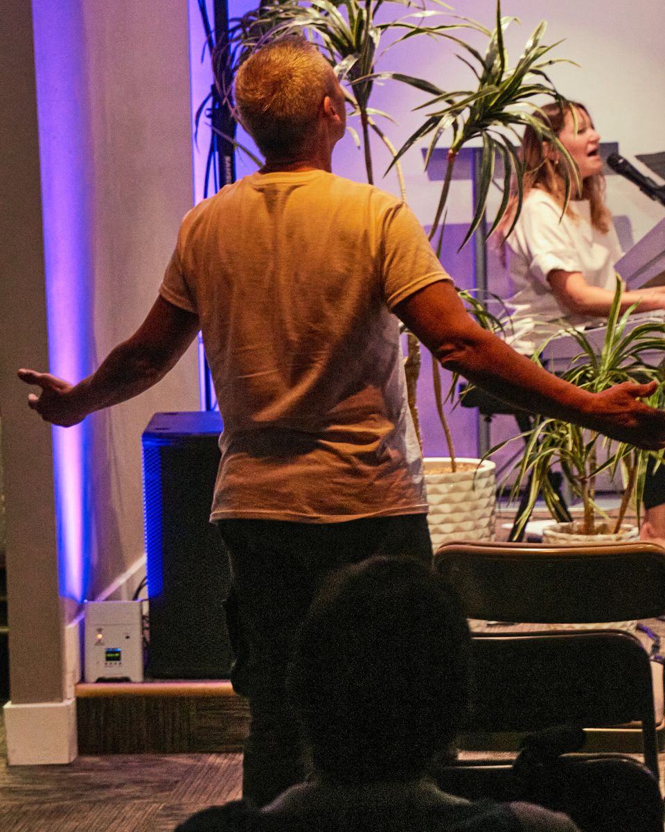 A man seen from behind with his arms outstretched; a keyboardist singing beyond