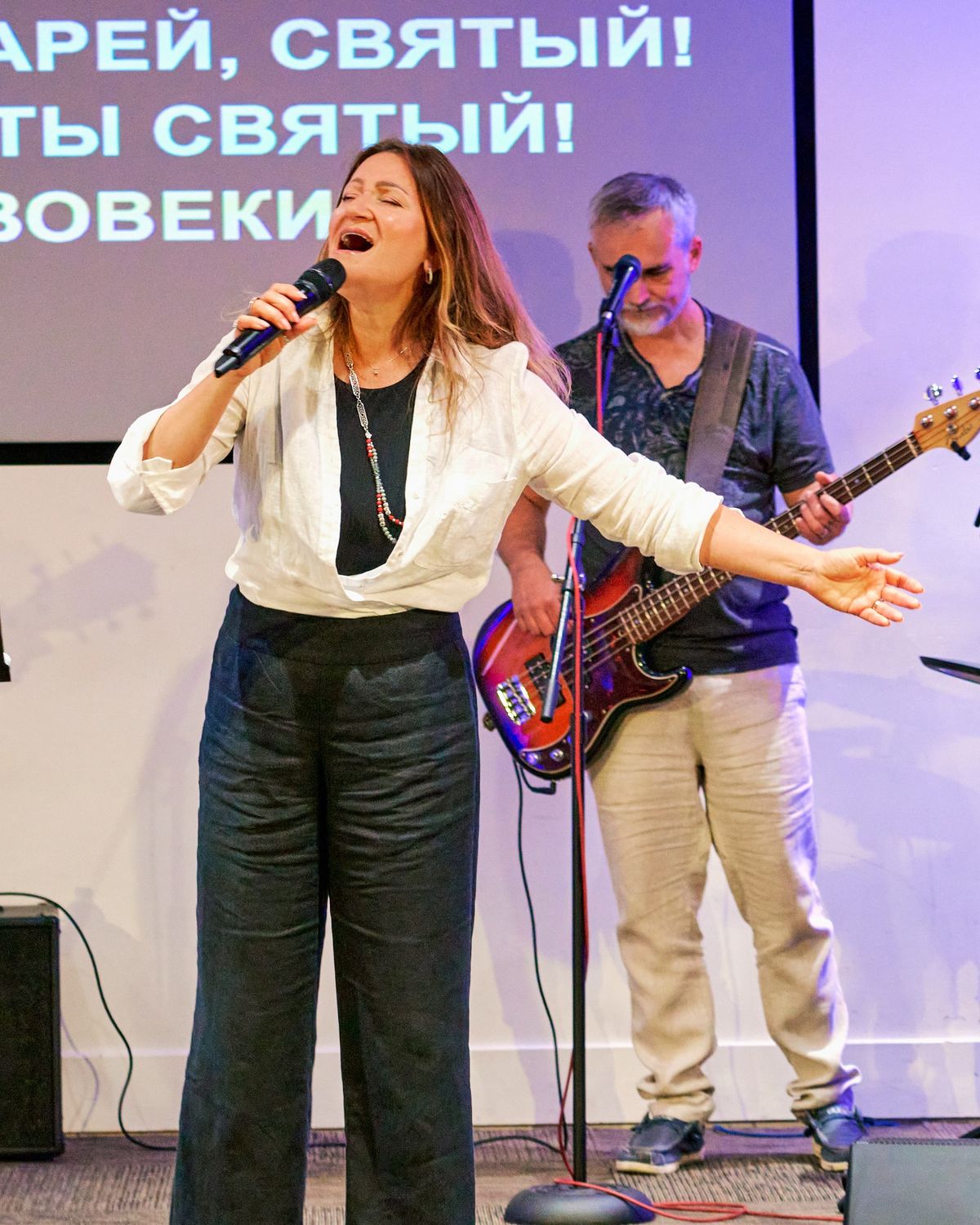 Певица ведёт прославление с микрофоном в руке; за ней басист